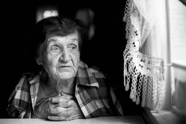 Anlamlı gözleri olan yaşlı bir kadın pencerenin yanında düşünceli bir şekilde oturur..