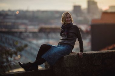 Portekiz, Porto 'da eski bir taş duvarda bir kadın oturuyor. Arka planda Dom Luis Köprüsü 'nün bulanıklığında.