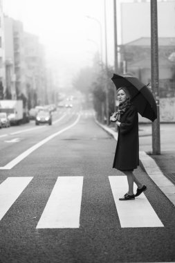 Şemsiyeli bir kadın siste yolun kenarında duruyor. Siyah beyaz fotoğraf.