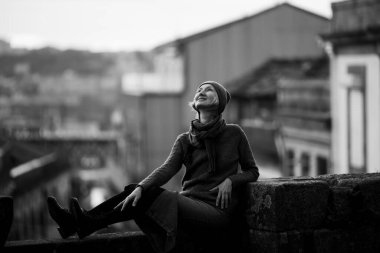 Portekiz, Porto 'da taş bir duvarda oturan bir kadın. Siyah beyaz fotoğraf.