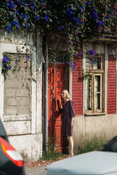 A woman stands outside the door of an abandoned house, knocks and listens.