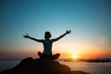 Silhouette woman yoga, practicing by the ocean during sunset.   