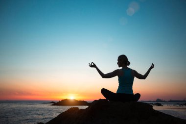 Silhouette yogi woman, practicing yoga in lotus pose on the beach during sunset.   