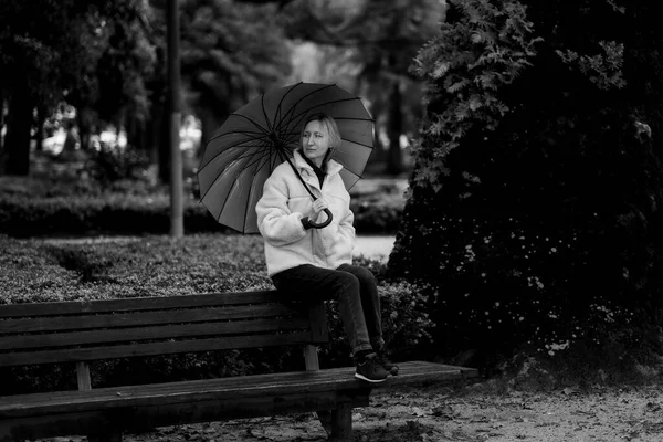 一个女人坐在公园的长椅上 拿着一把雨伞 黑白照片 — 图库照片