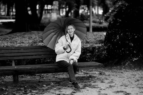 一个女人坐在公园的长椅上 拿着一把雨伞 看着摄像机 黑白照片 — 图库照片