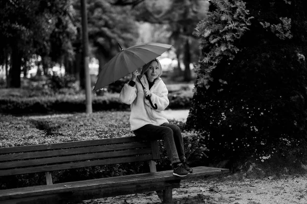 一个拿着雨伞的女人坐在公园的长椅上 黑白照片 — 图库照片