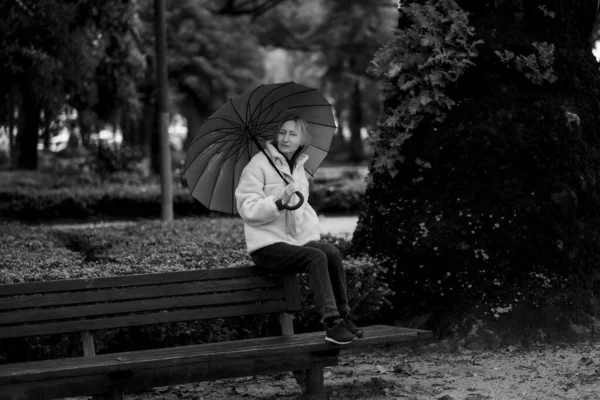 秋の公園のベンチに傘を差した女性 白黒写真 — ストック写真
