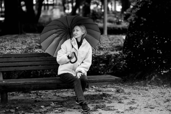 傘を差した女性が公園に腰を下ろしている 白黒写真 — ストック写真