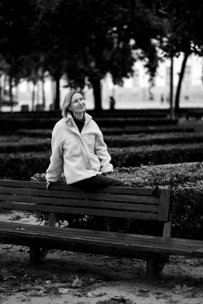 一个女人坐在公园长椅的后面 黑白照片 — 图库照片