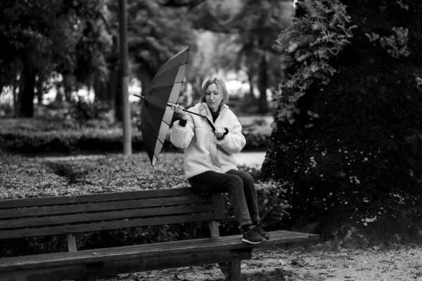 一个女人坐在公园的长椅上 雨天雨伞坏了 黑白照片 — 图库照片