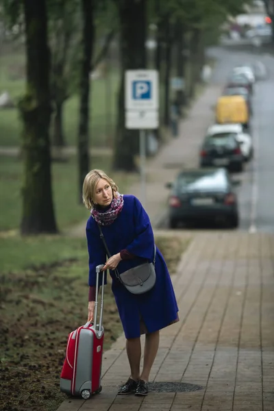 スーツケースを持った女性がタクシーを待って歩道に立って — ストック写真