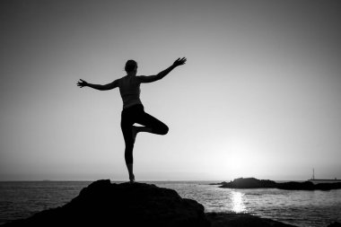 Güzel bir gün batımında okyanus kıyısında yoga yapan bir kadın. Siyah beyaz fotoğraf