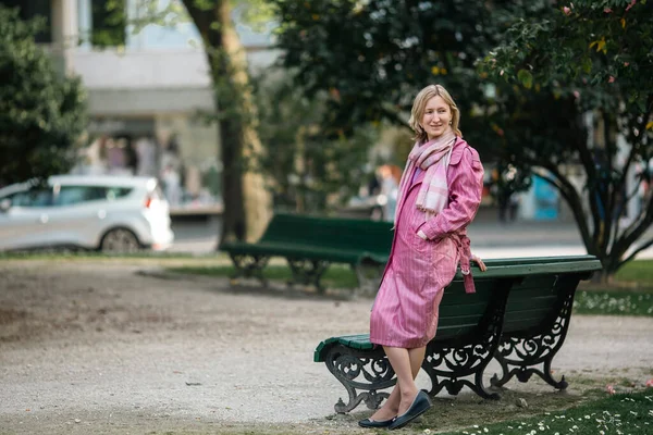 在公园里 一个穿着华丽雨衣的女人站在一条长椅旁边 — 图库照片