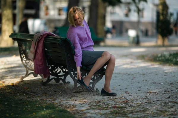 一个女人坐在长椅上 从鞋子里抖出一块鹅卵石 — 图库照片
