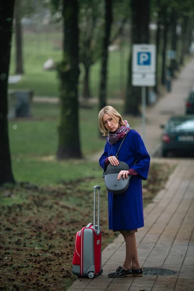 タクシーを待っている歩道にスーツケースを着た女性が立っている — ストック写真