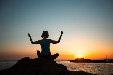 Gün batımında okyanus kıyısında poz veren bir kadının silüeti..