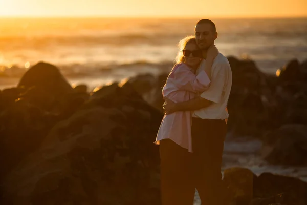 日落时分 一对年轻夫妇在岩石海岸浪漫地拥抱在一起 — 图库照片
