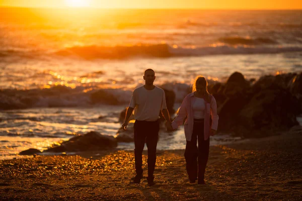 一对恋爱中的年轻夫妇在日落时在海边散步 — 图库照片