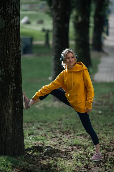 一个女人带着耳机在公园里暖身 然后在公园里慢跑 — 图库照片