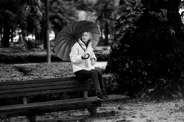 公园里一个拿着雨伞坐在长椅上的女人黑白照片 — 图库照片