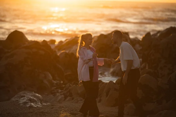 一对年轻夫妇在金色的夕阳西下的海滩上玩耍 — 图库照片