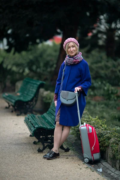 一个拿着红色手提箱的女人站在公园的一条长椅旁边 — 图库照片