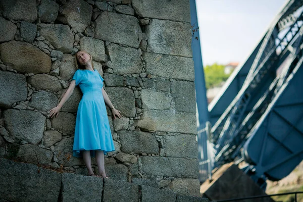 青いドレスを着た女性がポルトガルのポルトにあるエッフェル橋の近くの古代遺跡の壁に向かって押されています — ストック写真
