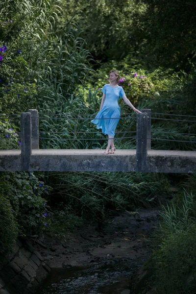 青いドレスの女性が古代の石の吊橋の上に立っている — ストック写真
