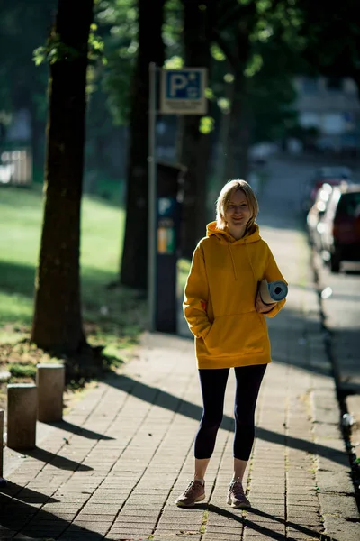 ヨガマットを持つ女性が街の公園を散歩する — ストック写真