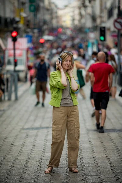 女性は混雑したストリートでヘッドフォンで音楽を楽しむ — ストック写真