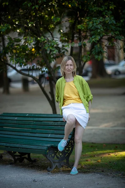 stock image A woman in a skirt sits on a park bench.