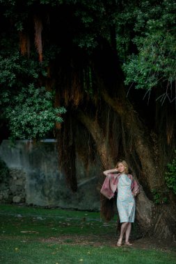 Parkta büyük bir ağacın yanında bir kadın duruyor..