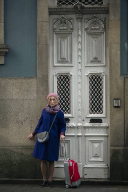 Geleneksel Portekiz kapılarının yanında kırmızı bavullu bir kadın..
