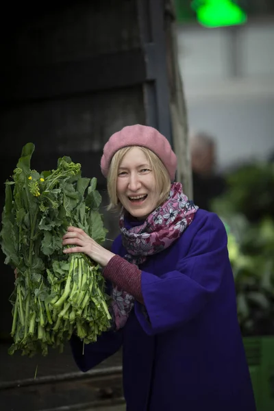A woman with greens in her hands in a vegetable shop.