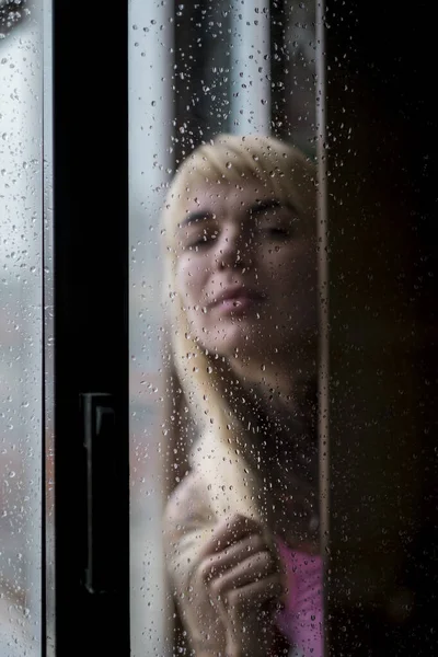 Portrait of a woman in blur in front of a window in raindrops.