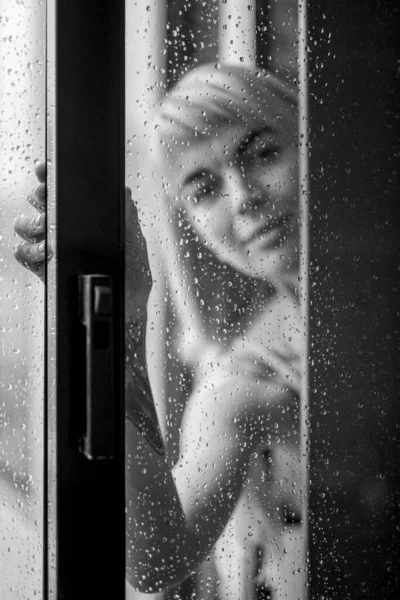 Woman in the window blur outside in raindrops. Black and white photo.