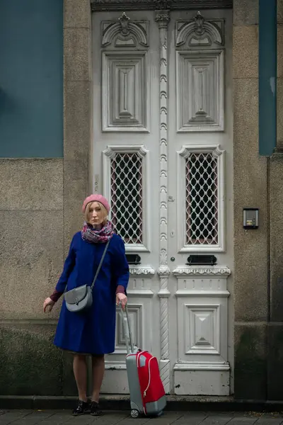 A woman with a suitcase stands at the front door of a building in Portugal.