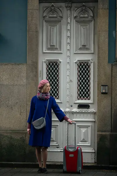 A woman with a suitcase stands at the front door of a traditional building in Porto, Portugal.