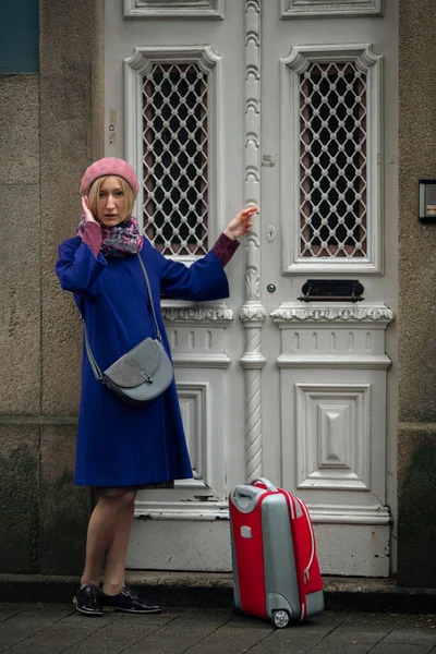 A woman with a suitcase knocks on the front door of a building in Porto, Portugal.