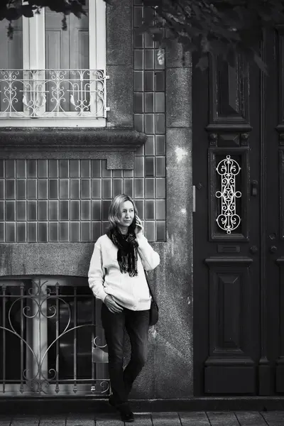 A woman calls her cell phone outside a traditional house on a street in Porto, Portugal. Black and white photo.