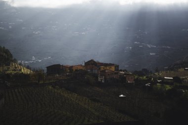 Bulutların arasındaki ışık Douro Vadisi 'nin tepelerindeki bir köyü aydınlatıyor. Portekiz.