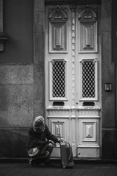 A woman with a suitcase near the door of a traditional house in Porto, Portugal. Black and white photo.