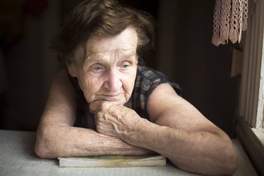 Üzgün yaşlı bir kadın bir evde oturuyor..