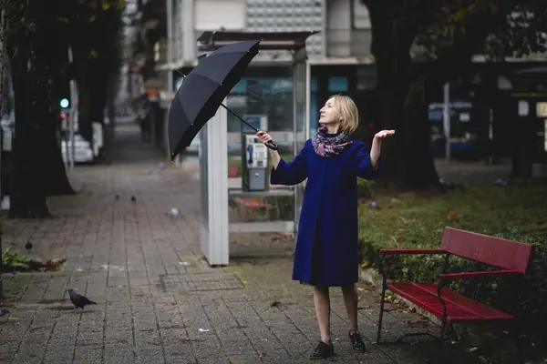 A woman opens an umbrella in the street.