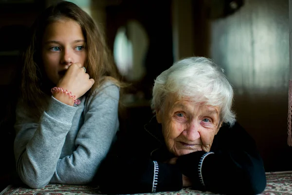 A portrait of an old grandmother, with a little girl granddaughter sitting next to her.