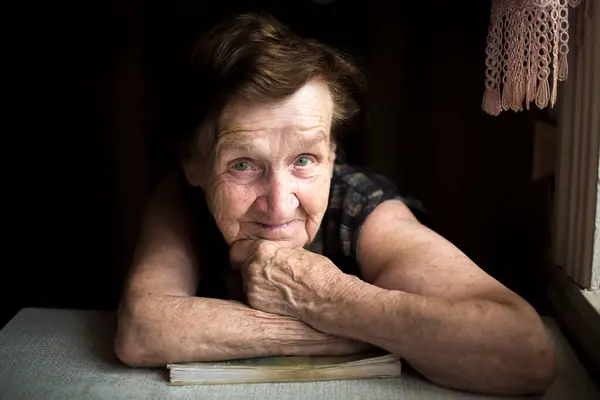一个满脸皱纹的老太太坐在一幢破房子里的画像 图库图片