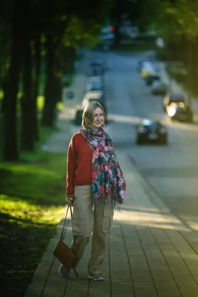 stock image A woman strolls along the tree-lined path in the park, enjoying the tranquil surroundings and the gentle rustle of leaves in the breeze.