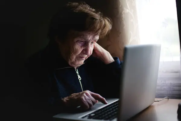在一个舒适的场景中 一位老太太舒服地使用她的笔记本电脑 把现代技术完美地融入她的日常工作中 图库图片