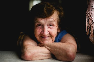 Yüzü nazik bir gülümsemeyle süslenmiş, sıcaklığı ve dayanıklılığı çağrıştıran yaşlı ve yalnız bir kadının yakın plan portresi..