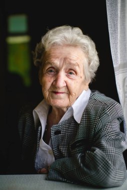 Yaşlı bir bayan masada oturur, bilgeliğini ve zarafetini yansıtan düşünceli bir portreye yakalanır..